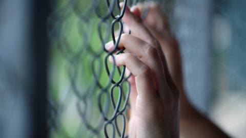 Hand holding onto detention fence